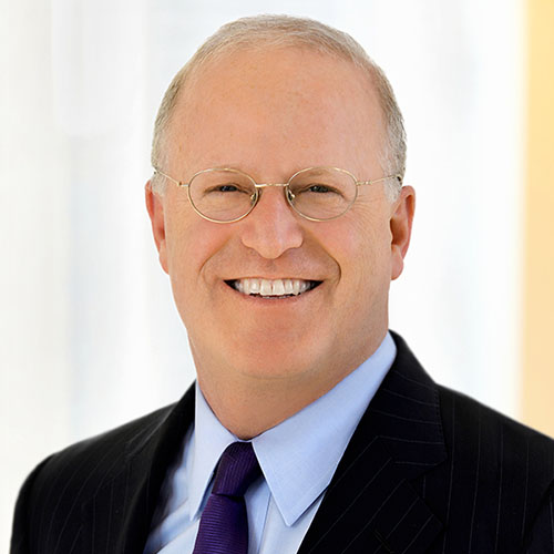Head shot of a smiling man with glasses wearing a suit and dark purple tie in front of a white background