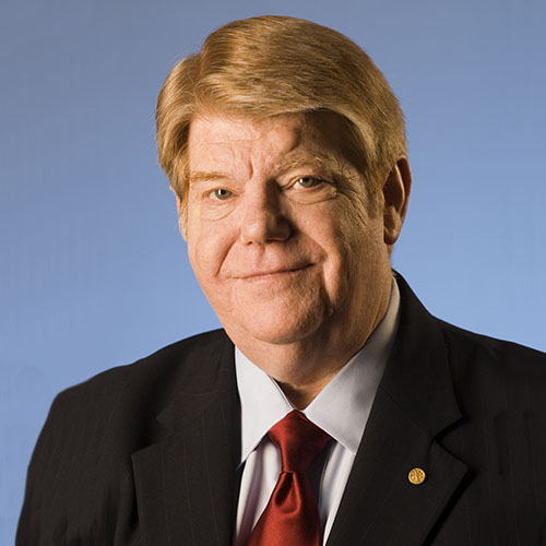 Headshot of a man with a red tie and suit in front of a blue background