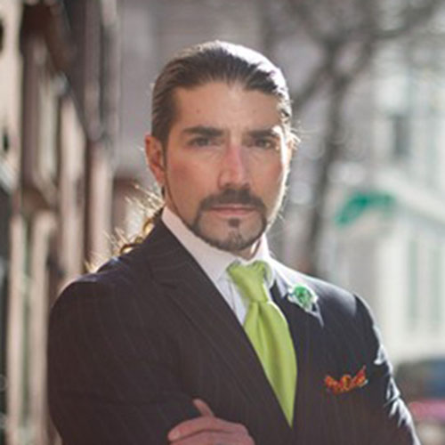 Head shot of a man in a suit with a lime green tie and his arms crossed