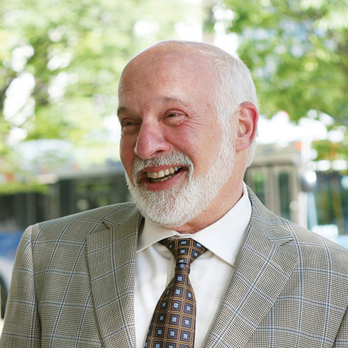 The Arc CEO Peter Berns smiles, looking off camera, in a plaid suit with trees in the background