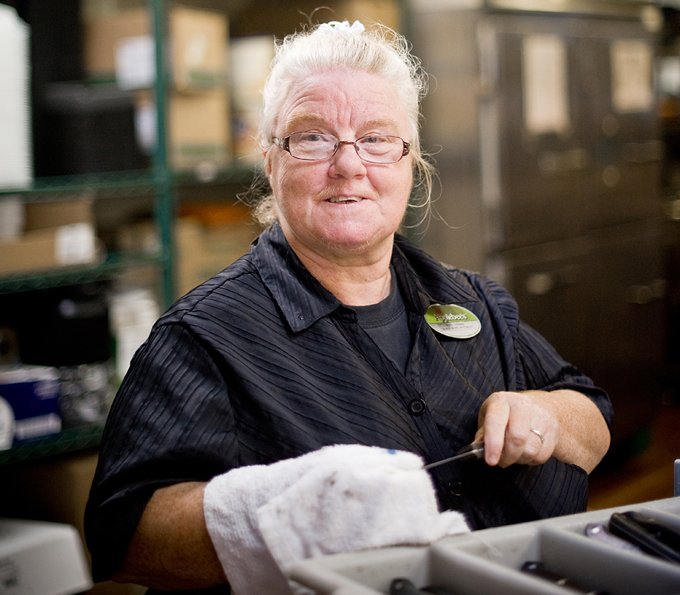 Older woman in a restaurant kitchen cleaning cutlery