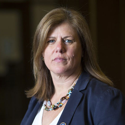 Headshot of a woman wearing a blue blazer in front of a dark brown background