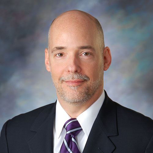 Head shot of a man in a suit and purple striped tie