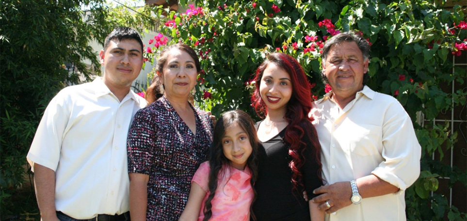 A family poses outside with a wall of flowers behind them