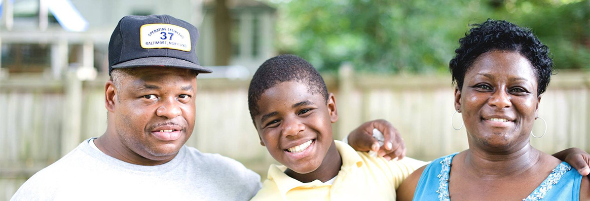 2-Values Portrait of African-American parents standing on either side of adolescent boy with trees and a fence in the background