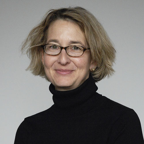 Head shot of a woman with glasses wearing a black turtleneck in front of a gray background