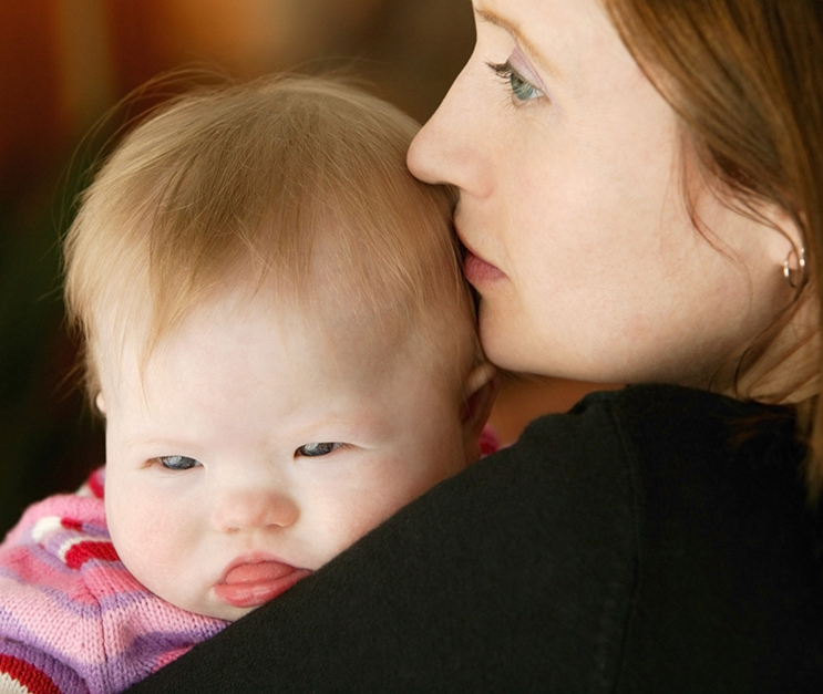 Close-up of mom holding baby with Down syndrome and looking off into the distance