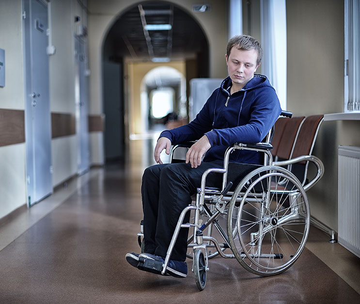 Young man in wheelchair looking down forlornly in empty hallway