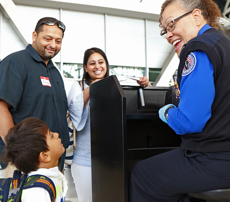 Small boy interacting with TSA professional at the airport while parents look on