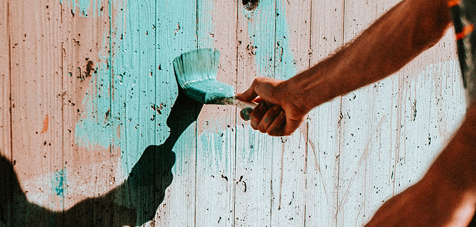 Hand holding paintbrush and painting a wooden wall teal blue