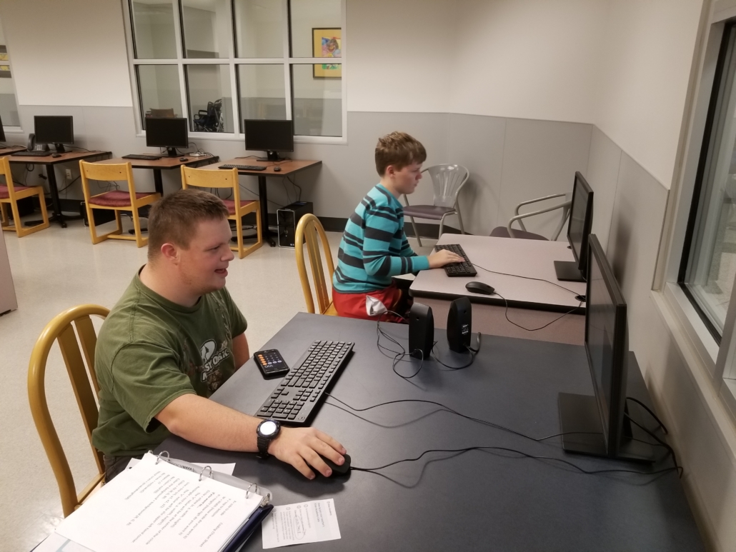 Two students sit in a computer lab in school, intently focused on their computer work.